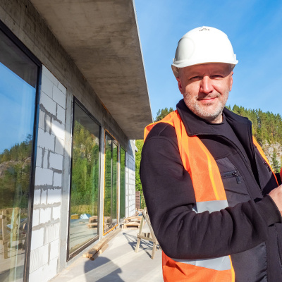 Energieberater mit gelben Helm und Bauunterlagen vor einem Haus